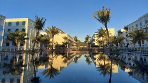 Un hotel con piscina reflectante, palmeras y arquitectura clásica.