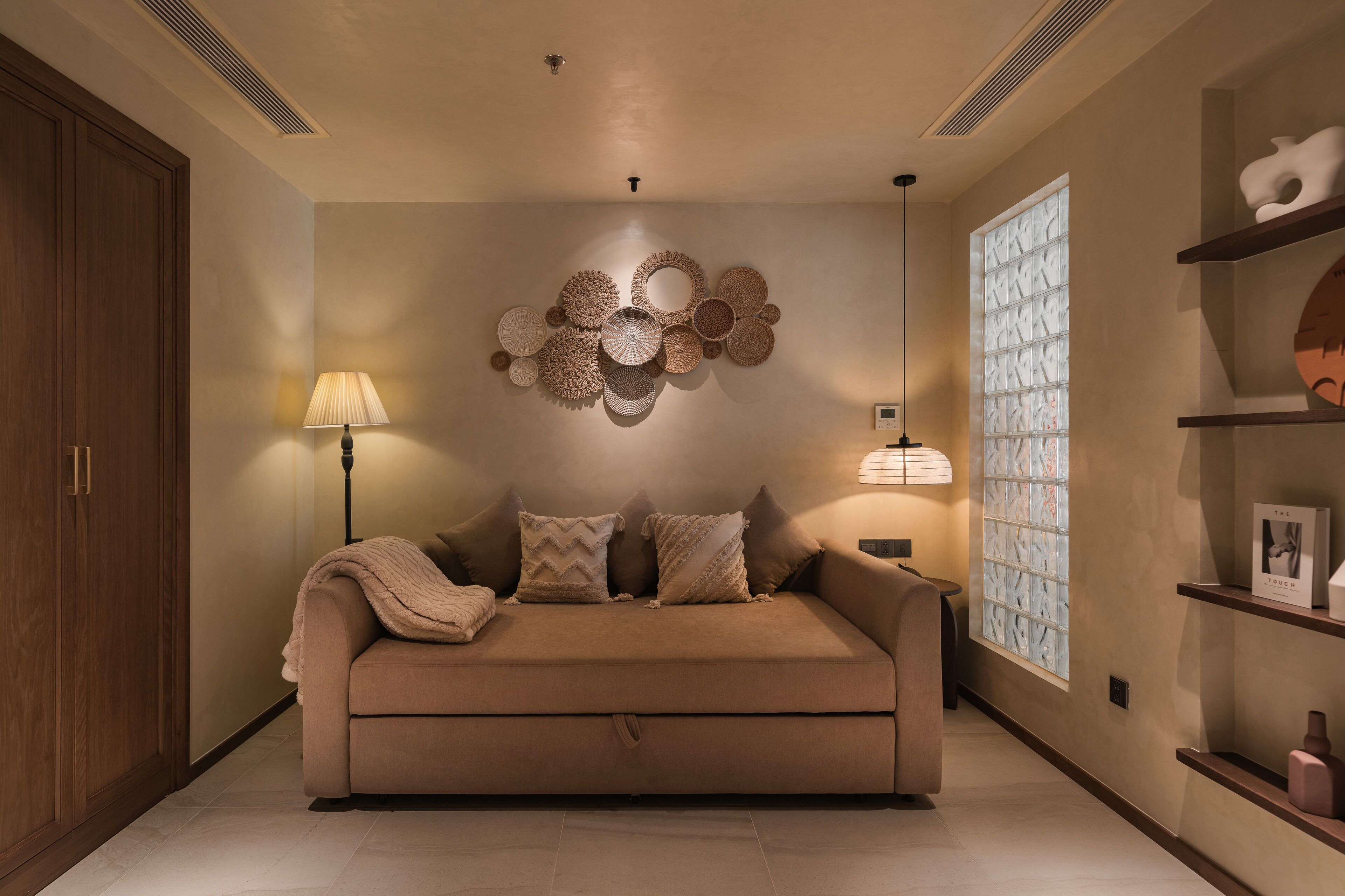 A modern living room with a beige sofa, patterned wall decor, and a large window with a geometric pattern.