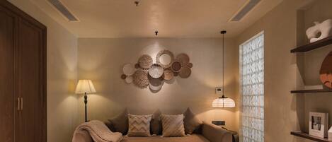 A modern living room with a beige sofa, patterned wall decor, and a large window with a geometric pattern.