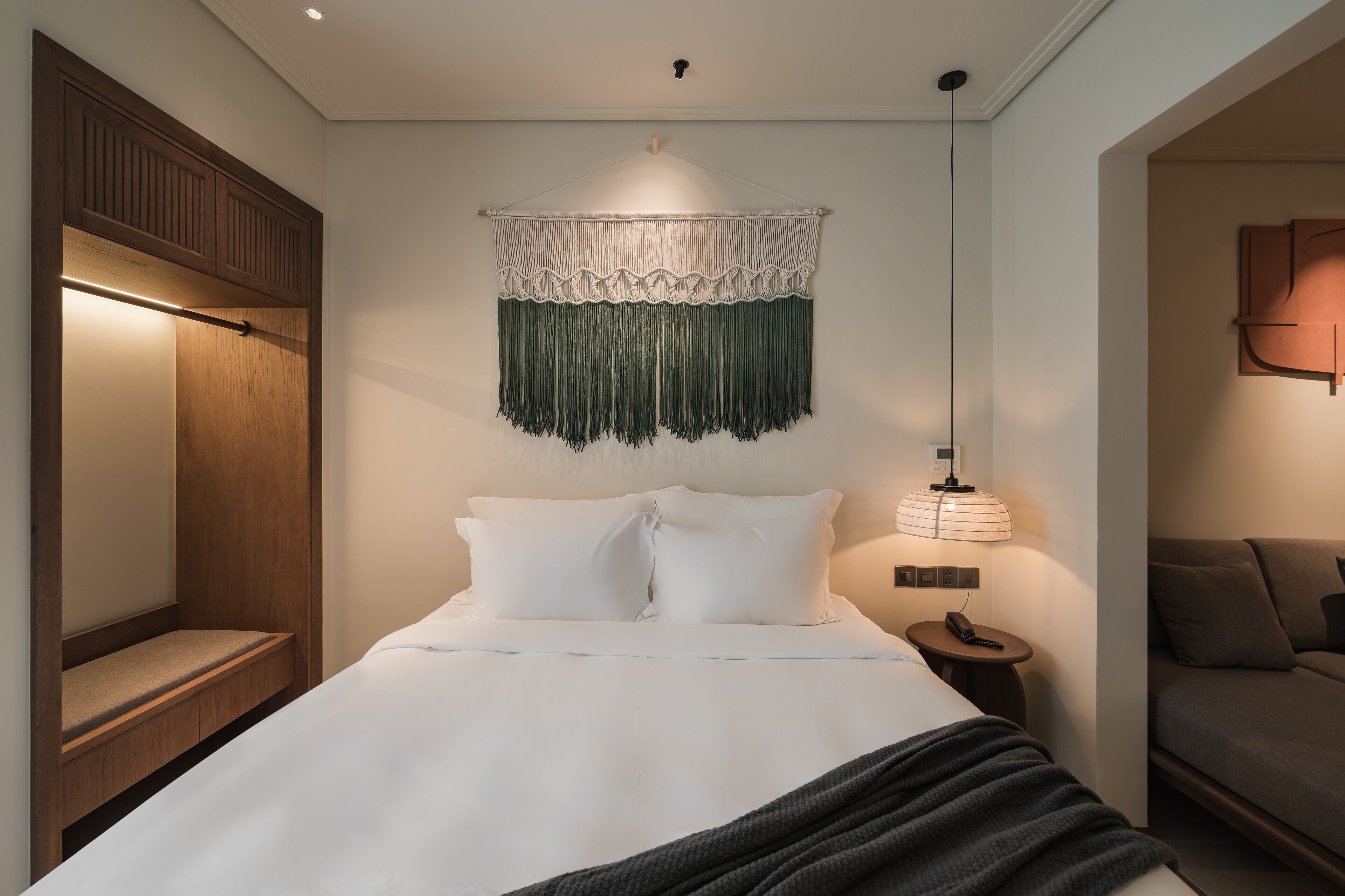 Een netjes opgemaakt slaapkamer met een bed, nachtkastje en een hangende macramé decoratie erboven.