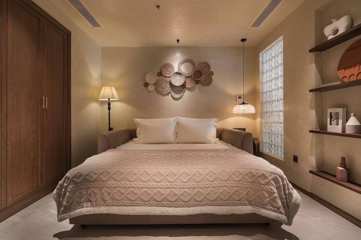 Un dormitorio con una cama grande, un armario de madera, un adorno en la pared y una ventana con persianas decorativas.