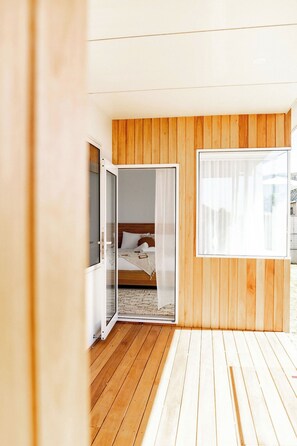 A bedroom with a wooden floor, a bed with white bedding, and a large window. - Ebenezer Bicheno - Discover the East Coast (Glamorgan-Spring Bay)