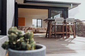 An outdoor deck with a table and chairs, a potted plant, and a view of the interior of a house.