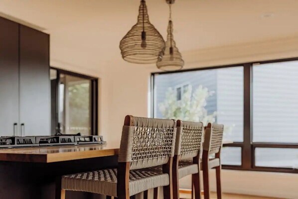 A modern kitchen with a central island, two hanging pendant lights, and a large window with a view of greenery.