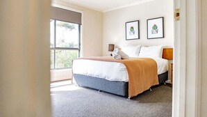 A bedroom with a large window, a bed with a white and brown bedspread, two framed pictures on the wall, and a nightstand with a lamp. - Allure Bicheno - Absolute Waterfront (Glamorgan-Spring Bay)