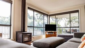 A modern living room with large windows, a fireplace, a flat-screen TV, and a grey sofa. - Allure Bicheno - Absolute Waterfront (Glamorgan-Spring Bay)