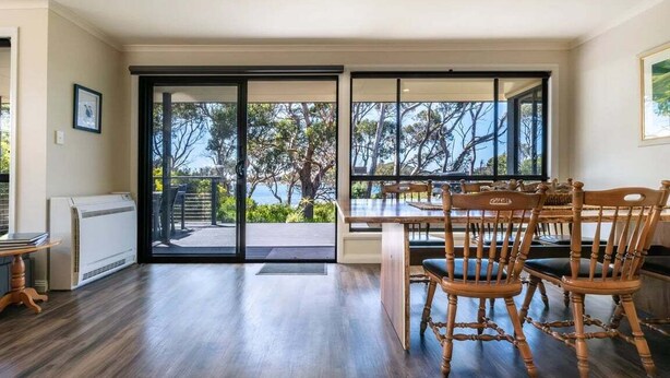 A dining area with a table and chairs, a view of the outdoors through large windows, and a sliding glass door leading to a patio. - Allure Bicheno - Absolute Waterfront (Glamorgan-Spring Bay)