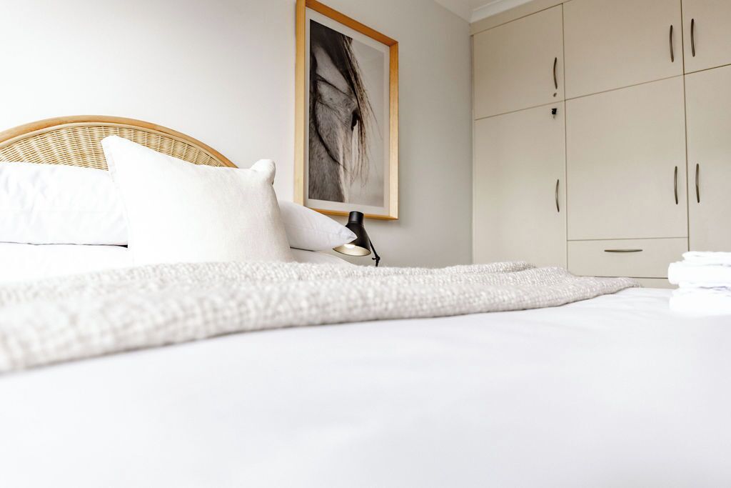 A neatly made bed with white linens, a white throw blanket, and a framed picture on the wall.