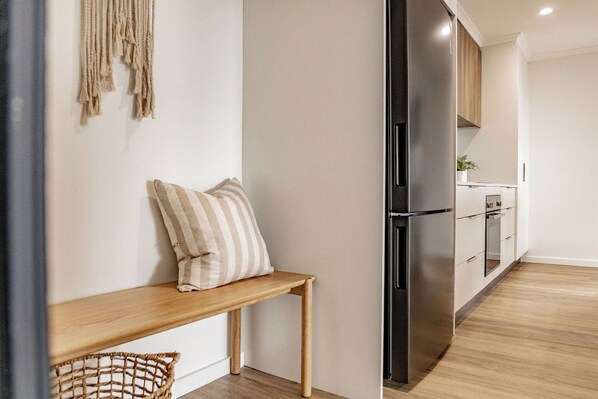Une cuisine moderne avec un réfrigérateur en acier inoxydable, des armoires en bois et un banc agrémenté d’un coussin à rayures.