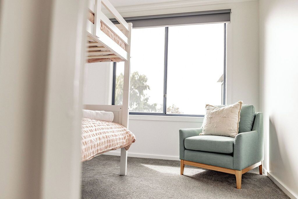 A child's bedroom with bunk beds, a green armchair, and a large window.