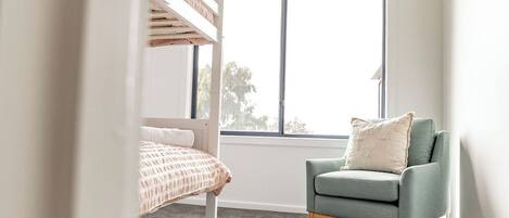 A child's bedroom with bunk beds, a green armchair, and a large window.