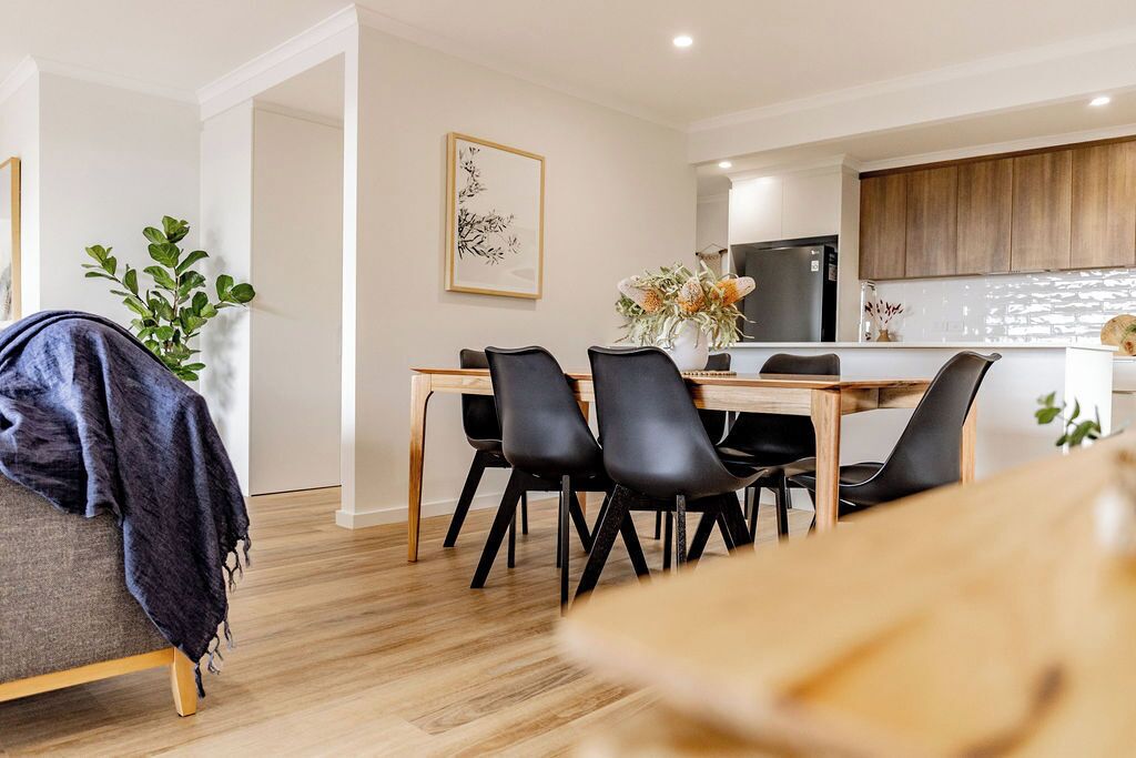 A modern kitchen with wooden cabinets, a black refrigerator, and a dining area with a wooden table and black chairs.