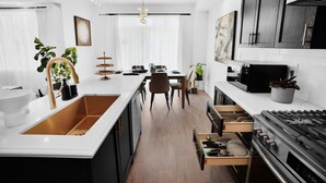 Cozinha moderna com ilha central, eletrodomésticos de aço inoxidável e área de jantar com lustre.