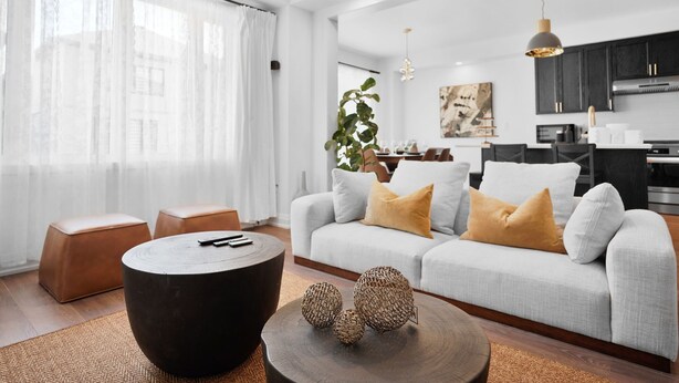 Uma sala de estar moderna com um sofá cinzento, uma mesa de centro redonda e uma área de jantar com uma mesa e cadeiras brancas.