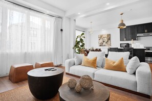 A modern living room with a grey sofa, round coffee table, and a dining area with a white table and chairs.