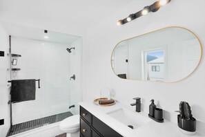 A modern bathroom with a glass shower enclosure, a white toilet, a black towel, a vanity with a mirror, and a sink with black fixtures. - Newly Renovated Modern Home near Niagara! (Thorold)