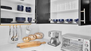 Uma cozinha com armários brancos, uma cafeteira, uma torradeira e diversos utensílios pendurados na parede.