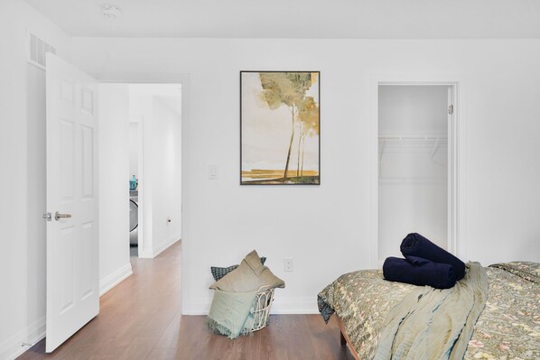 A bedroom with a bed, a painting on the wall, and a hallway leading to a bathroom.