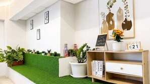Un área de recepción con piso de césped artificial verde, un escritorio de madera con un calendario y obras de arte enmarcadas en la pared.