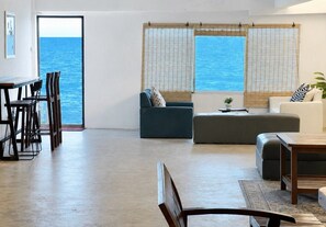Amplia sala de estar con vista al mar, un comedor con sillas y un sofá.