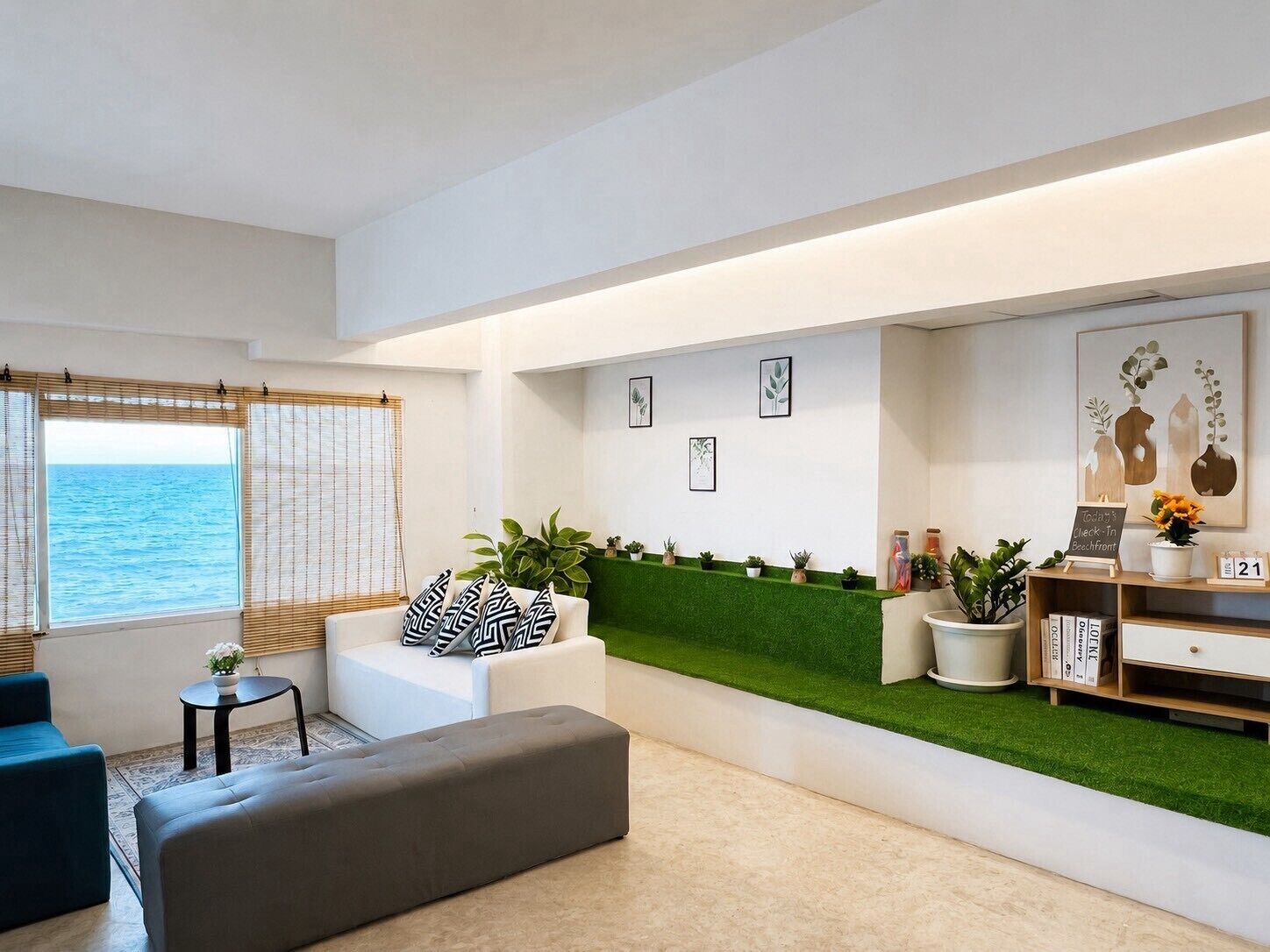 A modern living room with a sofa, ottoman, and a small table with a plant. There is a green wall with a shelf and a sign, and a window with a view of the sea.
