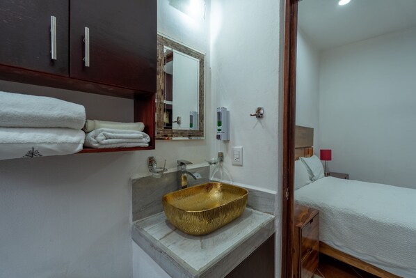 Une salle de bain avec un lavabo doré, des serviettes blanches, un miroir et un lit avec une lampe rouge.