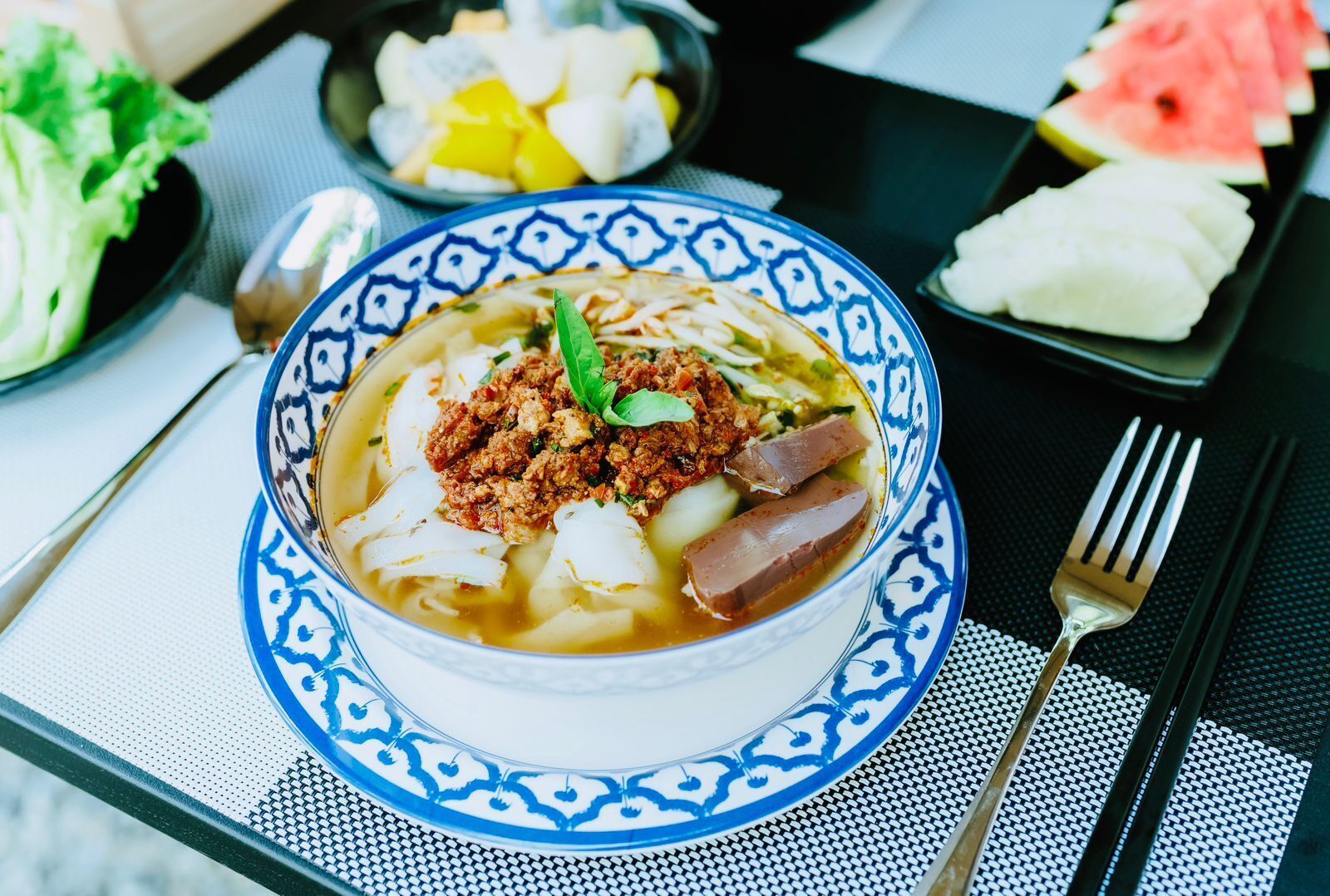 Un bol de soupe contenant de la viande et des légumes, posé sur une table avec une fourchette et une cuillère.