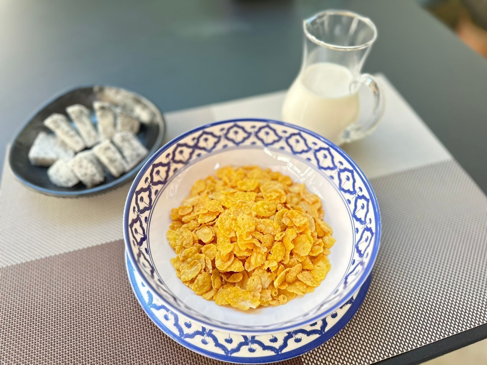 Un bol de céréales, une assiette de biscuits et un verre de lait sur une table.