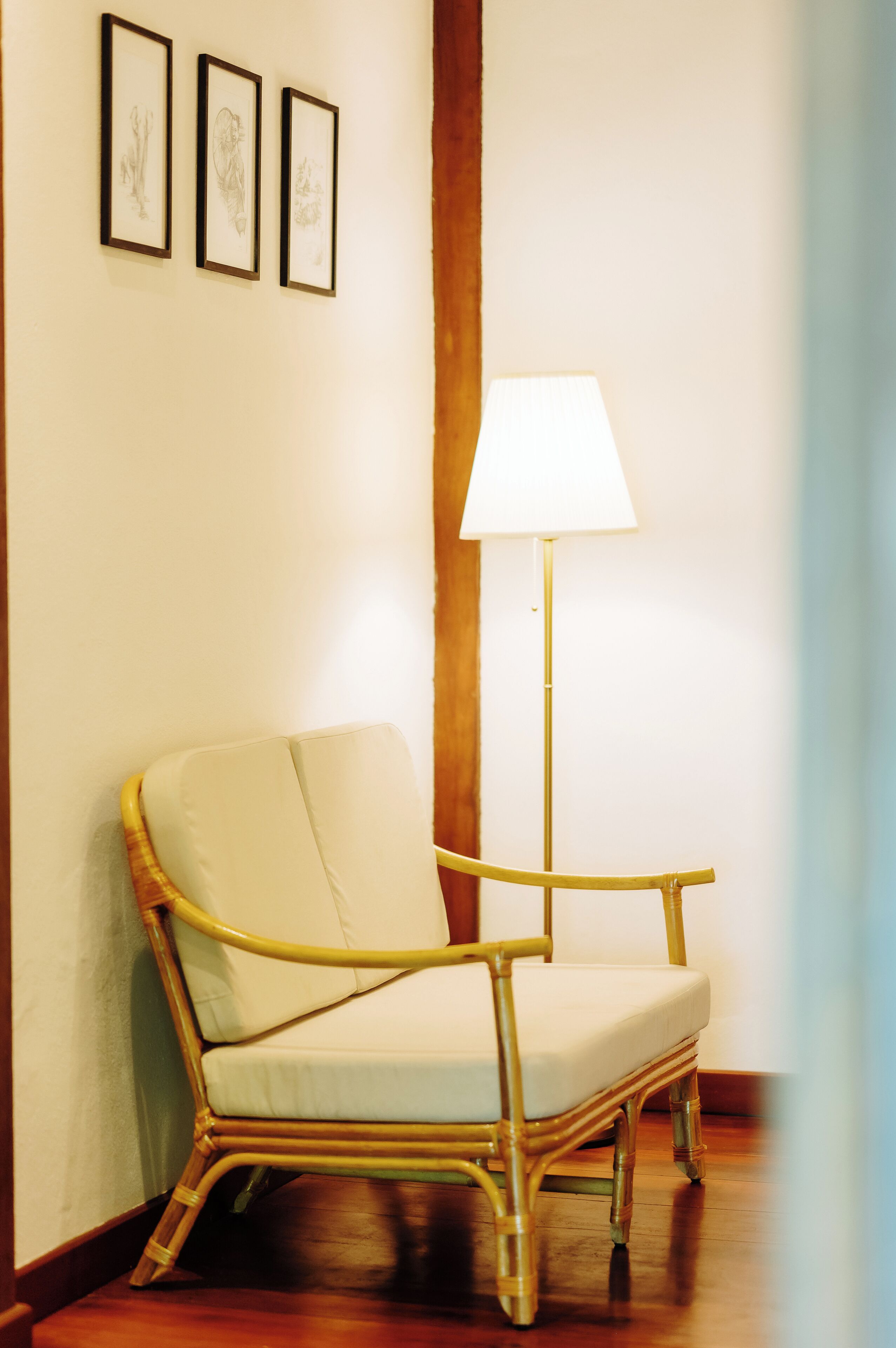 A wicker chair with a cushion, a floor lamp, and three framed artworks on the wall.