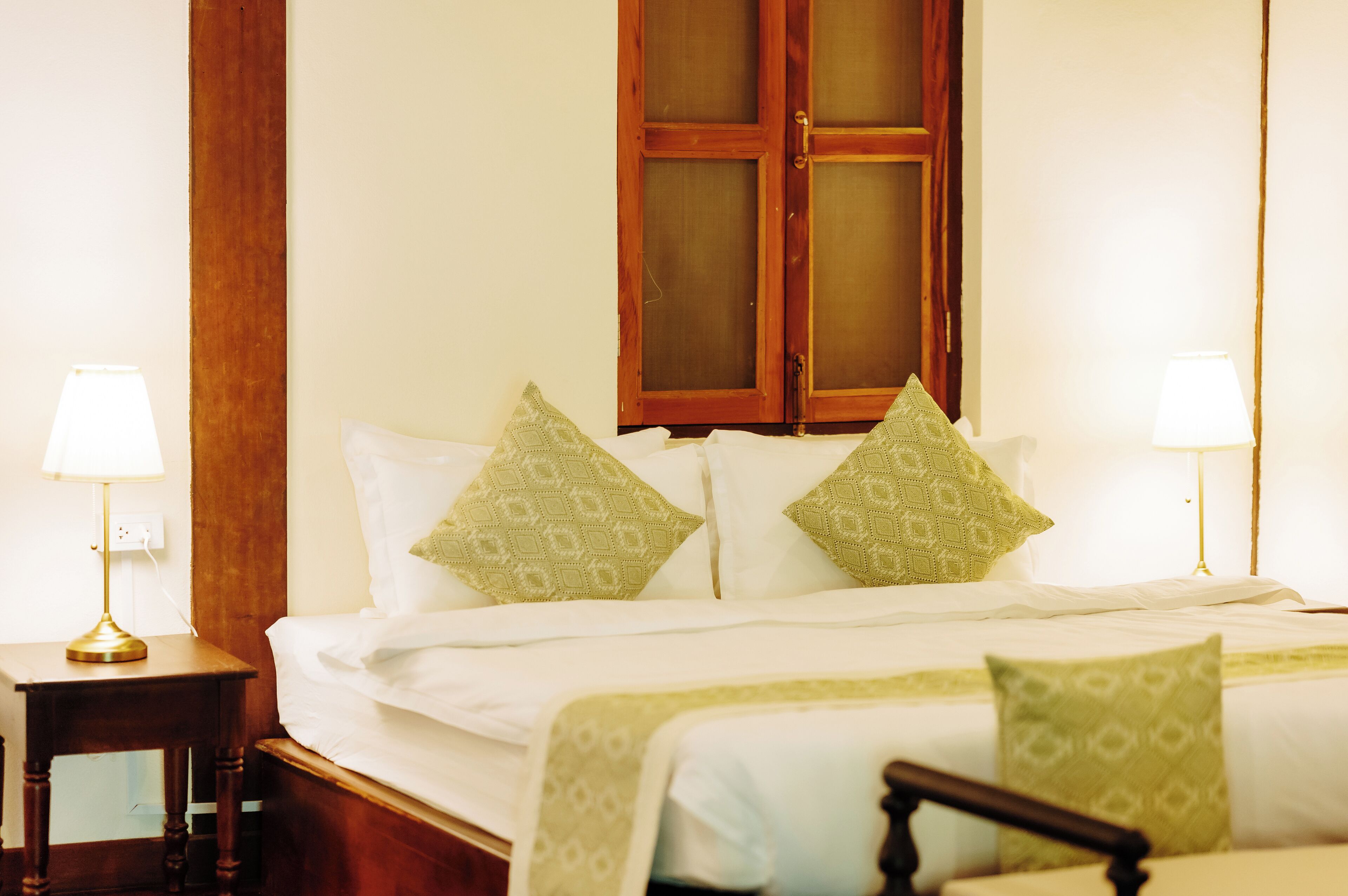 Una habitación de hotel con una cama de madera, dos lámparas de noche y un gran ventanal con contraventanas de madera.