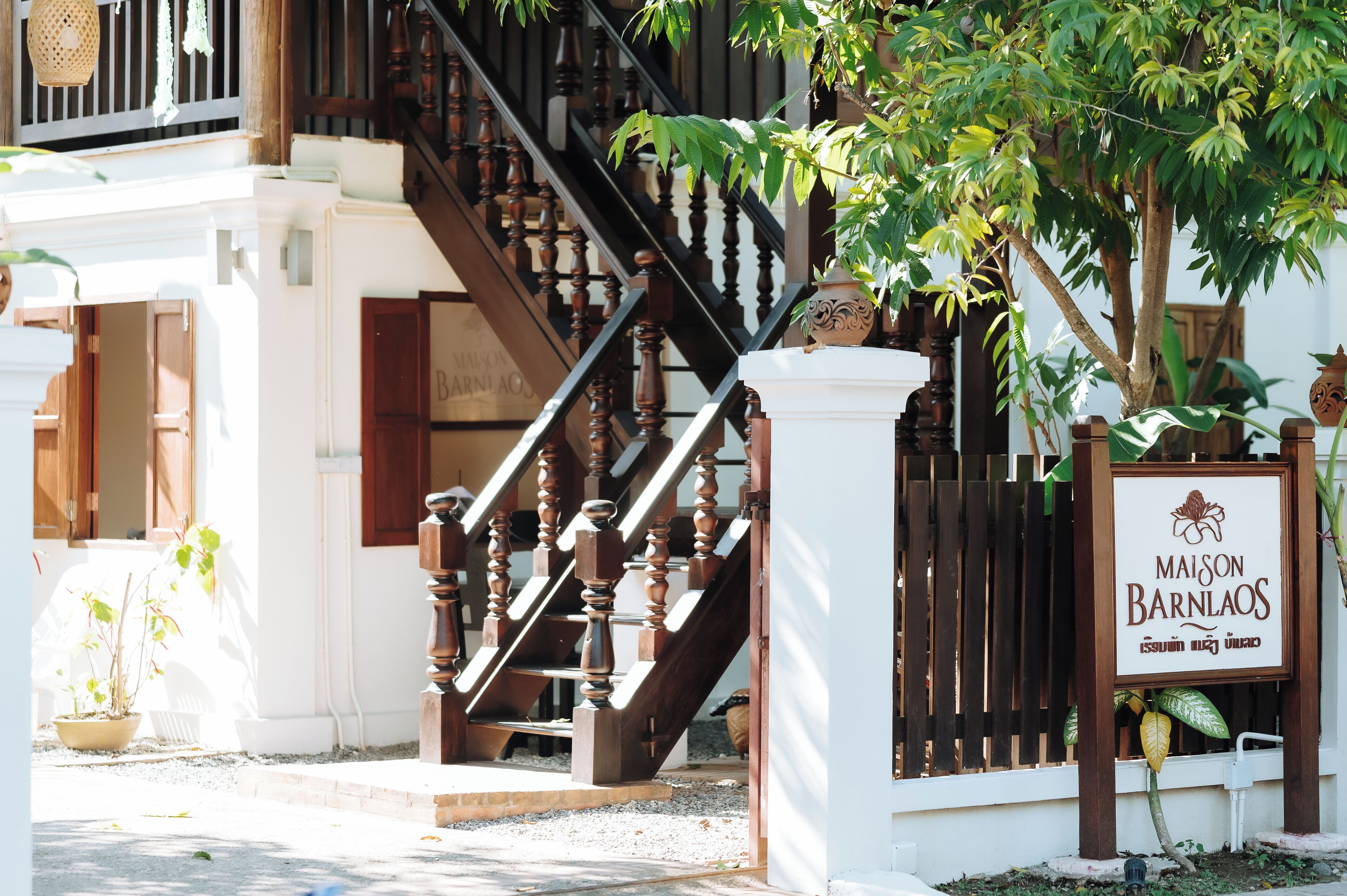 A staircase with wooden balusters leading to a white building with a sign reading "Maison Barnlaos".