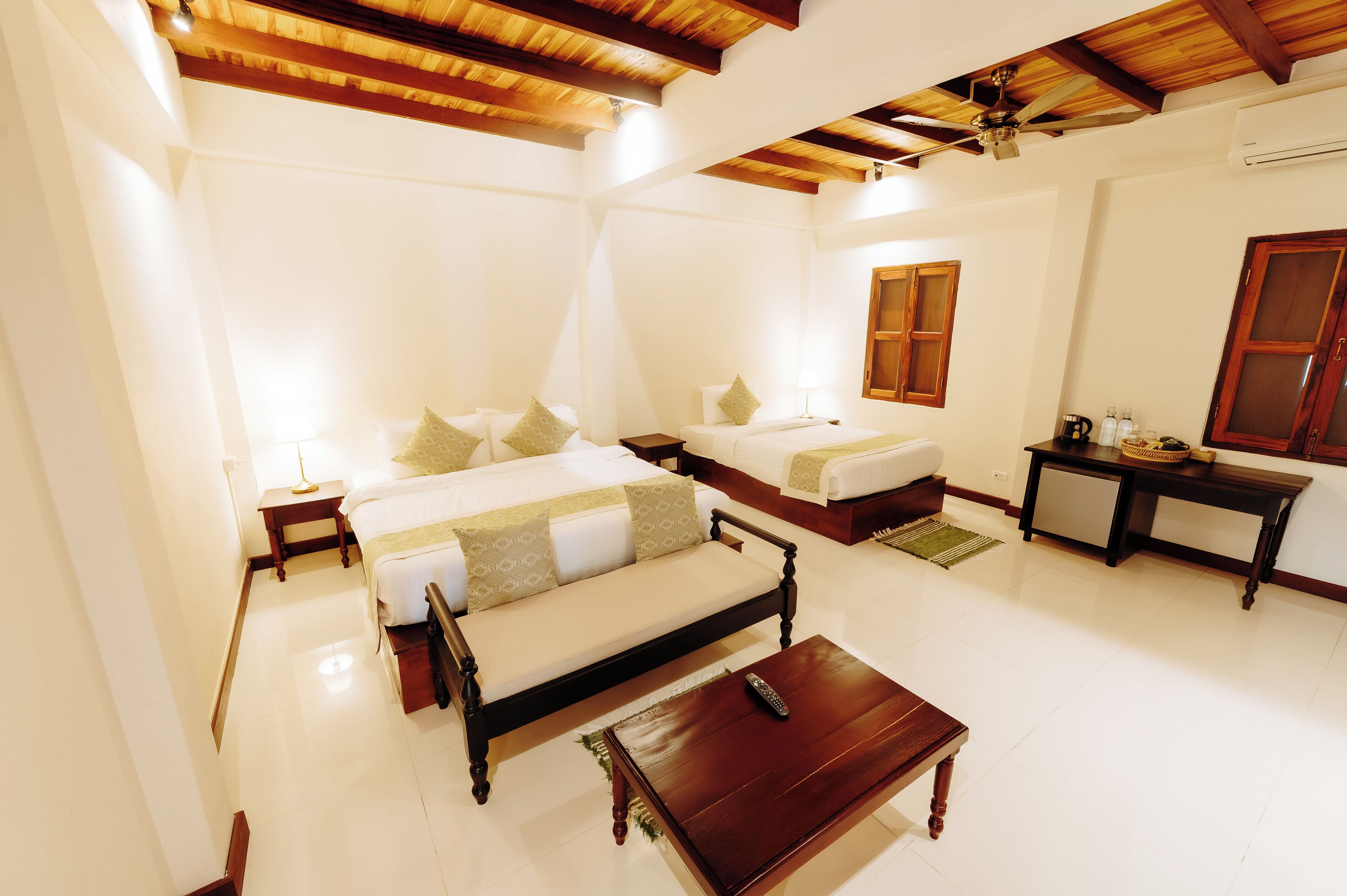 A hotel room with two beds, a wooden coffee table, a nightstand, and a small table with a lamp.