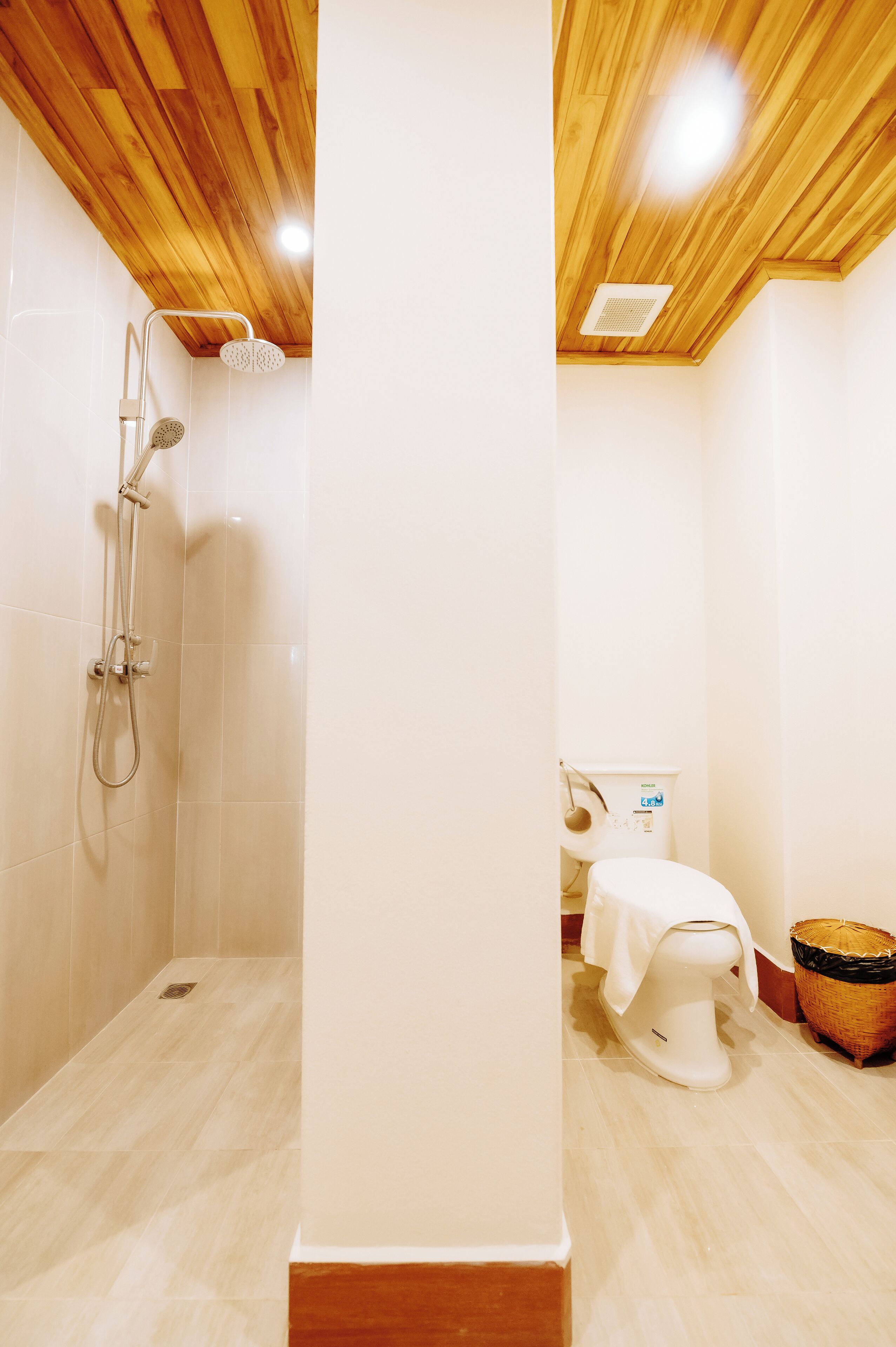 Eine Dusche mit Holzboden, eine Toilette mit weißem Deckel und ein Korb auf dem Boden.