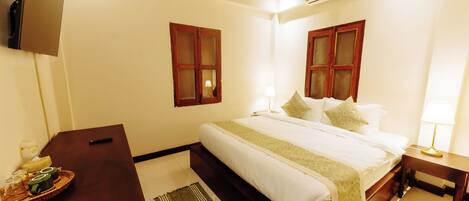 A bedroom with a bed, bedside tables, a desk, and a TV.