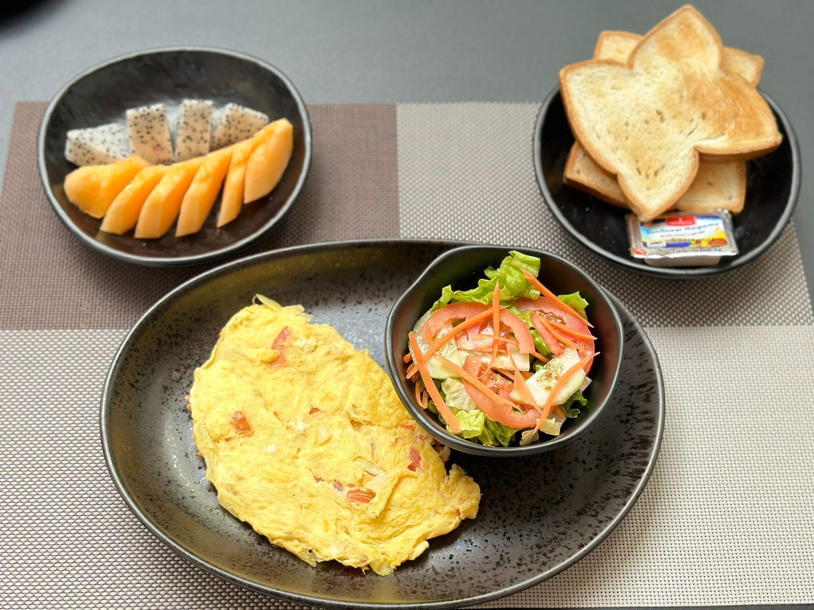 Un repas composé d’une omelette, d’une salade avec de la laitue et des tomates, et de deux assiettes contenant des toasts et un petit pot de beurre.