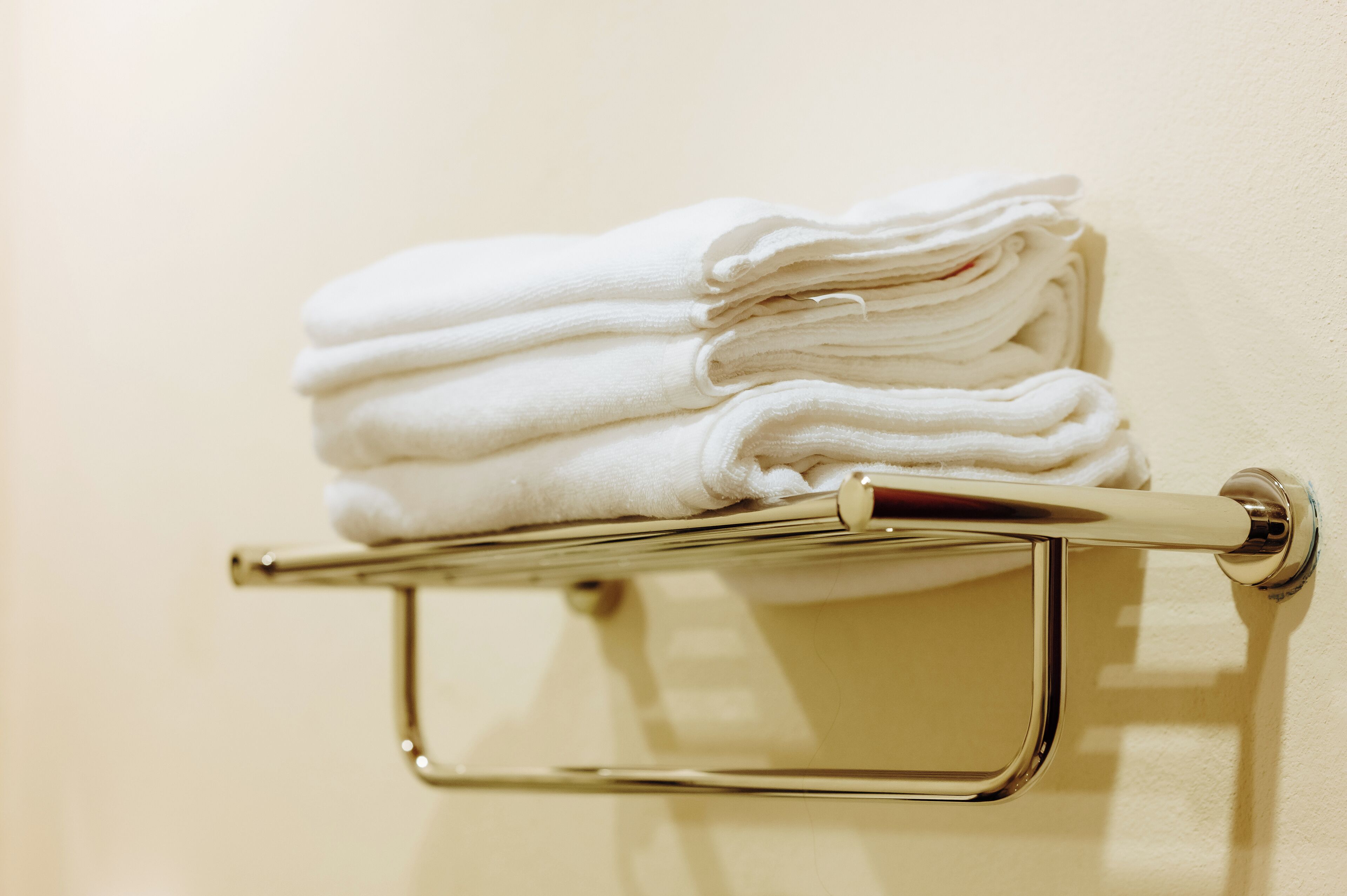 A stack of white towels on a metallic towel rack attached to a wall.