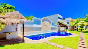A swimming pool with a stone wall, a thatched roof structure, and a paved walkway. - Gorgeous 8 People Basic Villa With Pool Playacar Phase 2 (Playa del Carmen)