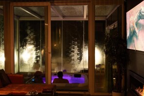 Quarto com porta de vidro que dá para uma área com hidromassagem, um sofá e uma lareira.