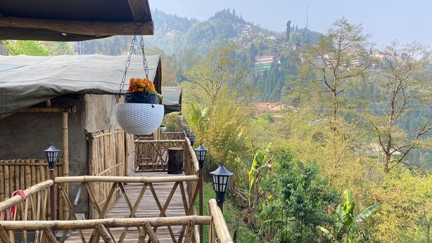 A wooden bridge with hanging baskets of flowers, leading to a building with a covered entrance. - Deoja Forest Stay (Darjeeling)