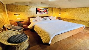 A cozy room with a bed, two wall-mounted lamps, a framed artwork, and a wicker chair. - Deoja Forest Stay (Darjeeling)