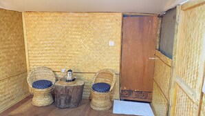 A room with two wicker chairs, a small wooden table with a kettle, and a wooden door. - Deoja Forest Stay (Darjeeling)