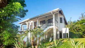 A two-story house with a balcony, surrounded by lush greenery.