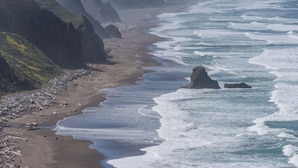 A coastal landscape with cliffs, a sandy beach, and waves crashing onto the shore. - Oceanfront/ Stunning Views/ Hot Tub/ Contemporary (Manchester)
