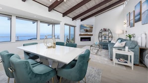 A spacious living area with a large white table, teal chairs, a fireplace, and a view of the ocean. - Oceanfront/ Stunning Views/ Hot Tub/ Contemporary (Manchester)