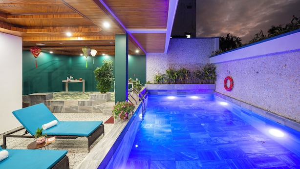 An indoor swimming pool with blue-tiled flooring, lounge chairs, and a small table with a plant. - May Boutique Villa Hoi An (Da Nang)