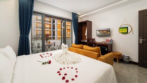 A hotel room with a bed, a desk, a chair, a TV, and a view of a building through the window. - May Boutique Villa Hoi An (Da Nang)