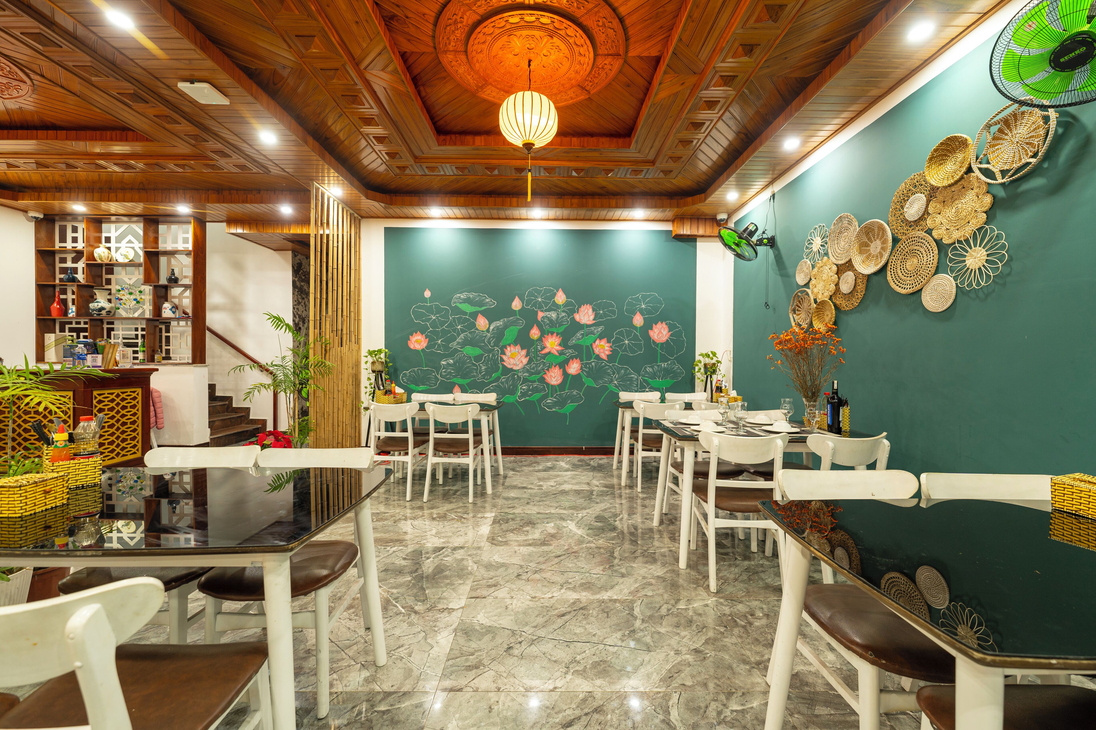 Een restaurant met een groene wand, houten plafond en een kroonluchter. Tafels en stoelen staan klaar voor diners.