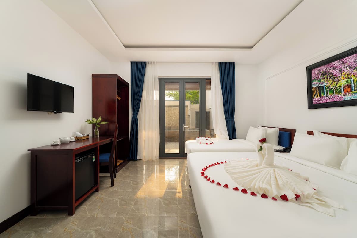 Une chambre d’hôtel équipée d’un téléviseur à écran plat, d’un bureau agrémenté d’une plante, d’un lit parsemé de pétales de rose et d’un tableau accroché au mur.