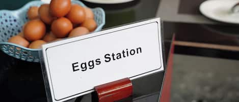 Letrero que indica 'Eggs Station', con una cesta de huevos y una fruta verde sobre una mesa.