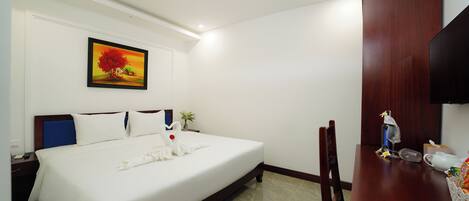 A hotel room with a bed, a desk, a chair, a television, and a painting on the wall.
